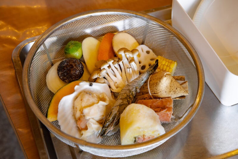 A metal colander containing assorted vegetables, mushrooms, lotus root, shrimp, shellfish, and other seafood from Oita is placed on a tray. The fresh ingredients are beautifully arranged—a must-try dish when deciding what to eat in Oita.