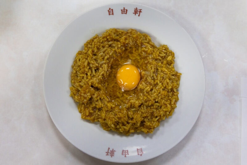 A must-try from the Osaka food guide: curry rice topped with a raw egg yolk, artfully served on a white dish adorned with red Chinese characters, captured from above.