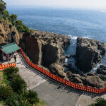 Udo Shrine: Miyazaki's Seaside Shrine The Udo Shrine, a scenic seaside shrine in Miyazaki, features a green roof perched atop rocky cliffs, framed by orange railings and lush greenery, offering breathtaking ocean views under a clear sky.