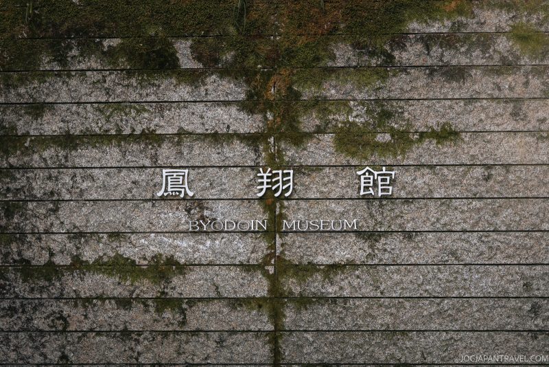 A stone wall with mossy green streaks features Japanese kanji and the words Byodoin Museum engraved in white letters, reflecting the historic charm of Byodoin Temple in Uji, Kyoto.